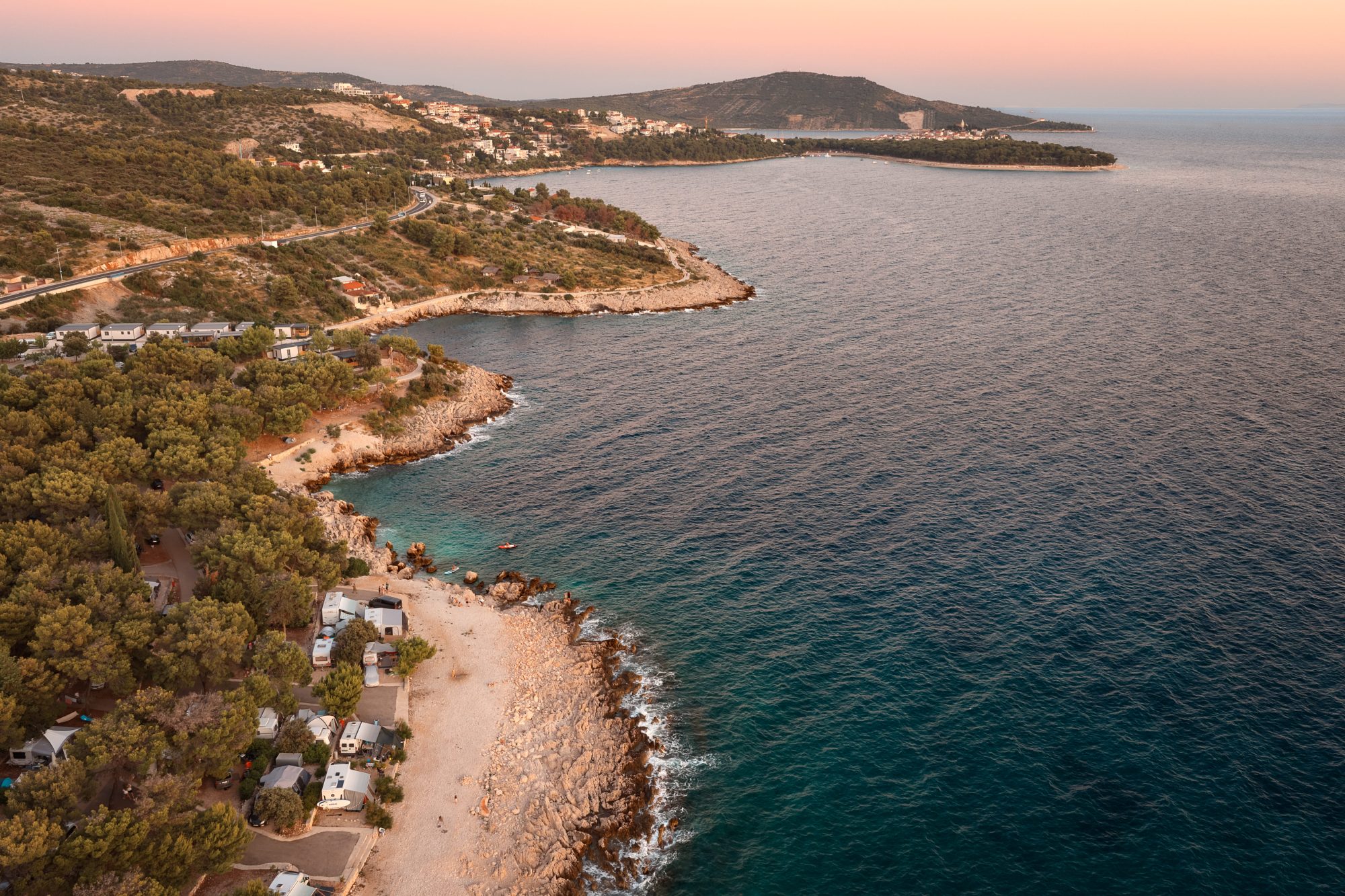 Aerial view of a pine-lined Adriatic coastline and seaside camp at sunset